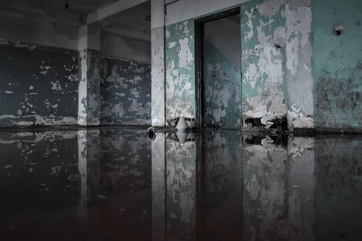 An empty room with peeling paint and standing water covering the floor.