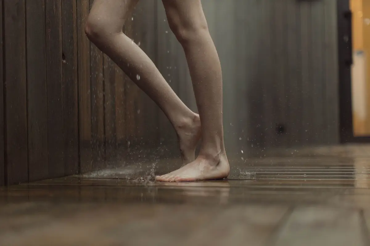 Bare feet standing on a wet wooden floor inside a house.